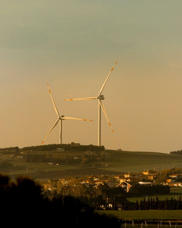 Scenic view of wind turbines on a hill near a rural village, capturing renewable energy beauty.